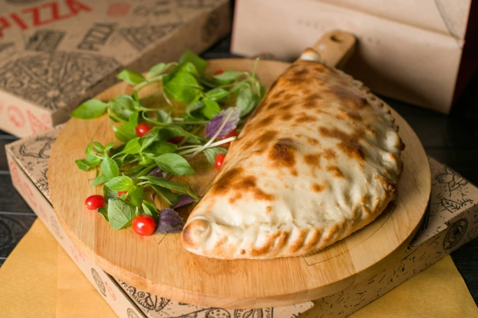 A delicious calzone sits on a wooden board.
